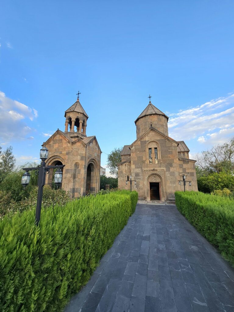 A historic Armenian church under blue skies amidst lush greenery.